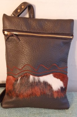 Denne taske er af sort skind med pynt af en strimmel broget ko skind og lidt pyntesyninger. Størrelse 20 x 30 cm